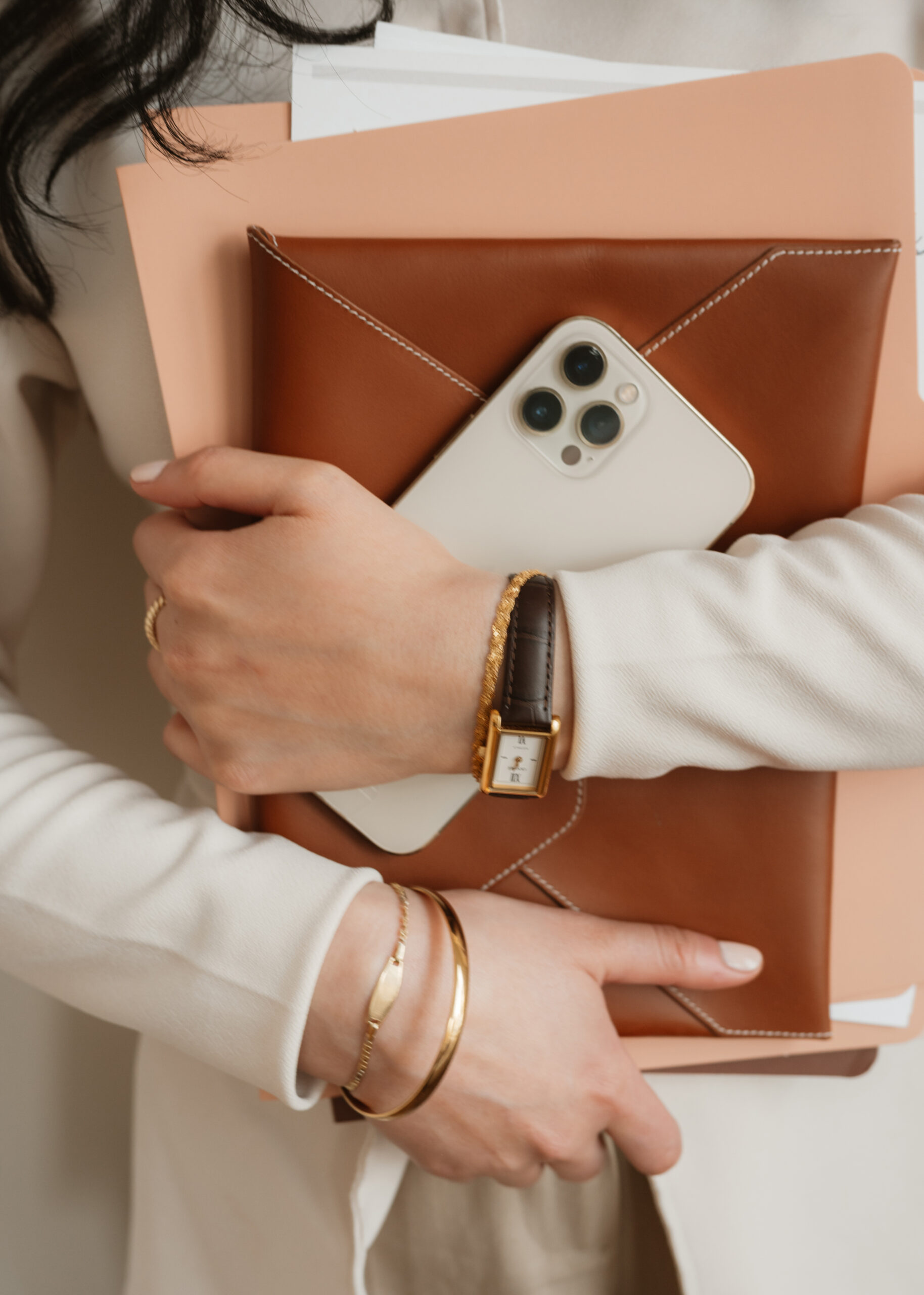 Woman holding a leather portfolio, folders, and smartphone in a neutral professional setting