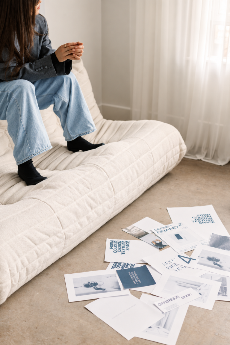 A creative professional seated beside printed brand layouts and photographs spread across the floor.