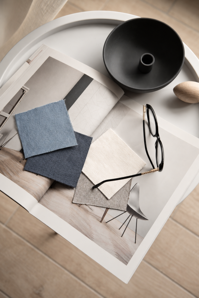 Open laptop beside tortoiseshell glasses and powder-blue, slate, and cream fabric swatches on a light wood desk.