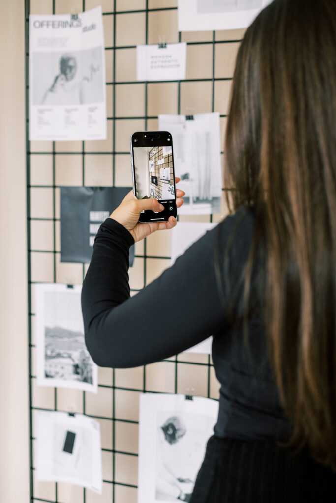 Woman using a smartphone to photograph printed references attached to a black wire grid.