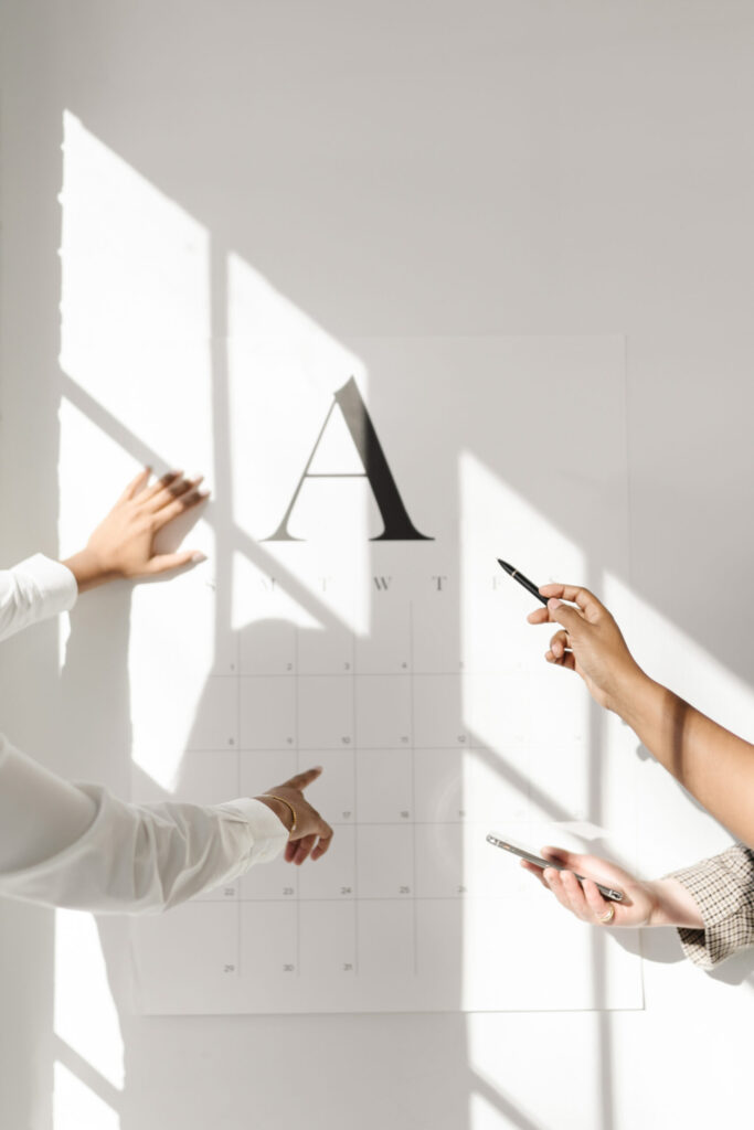 Team members planning around a wall calendar in a bright, sunlit office.