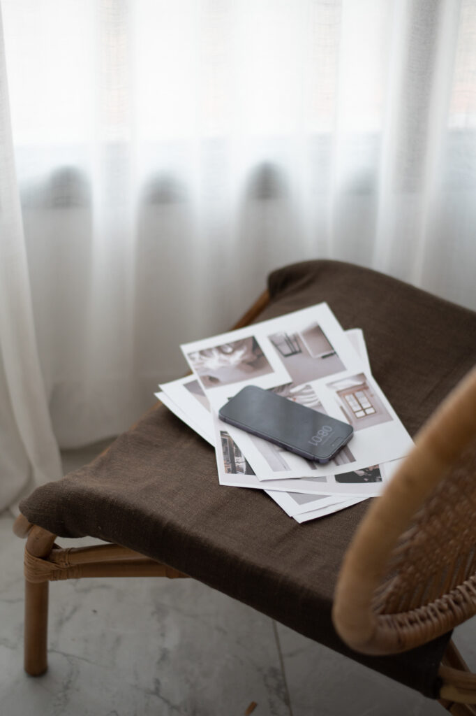Smartphone resting on a stack of printed reference photographs arranged on a brown upholstered chair.
