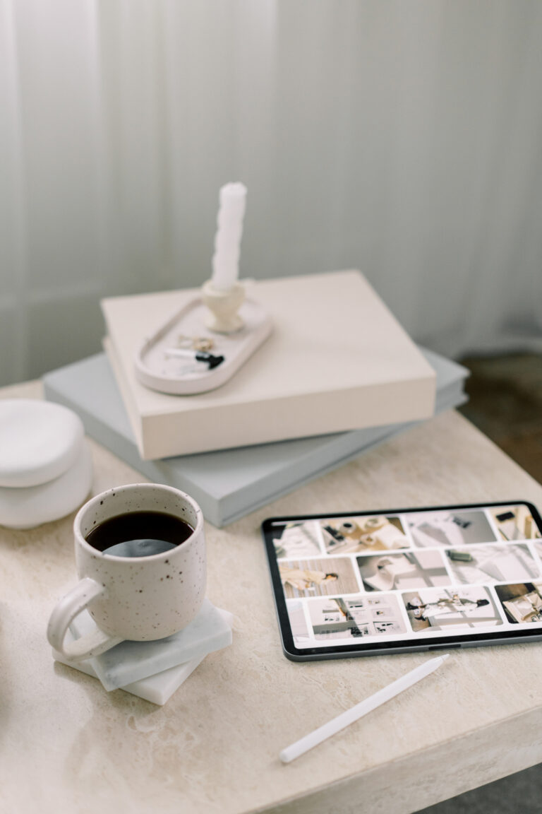 Tablet displaying visual references beside a ceramic mug of coffee, stacked books, a white stylus, and a candle.