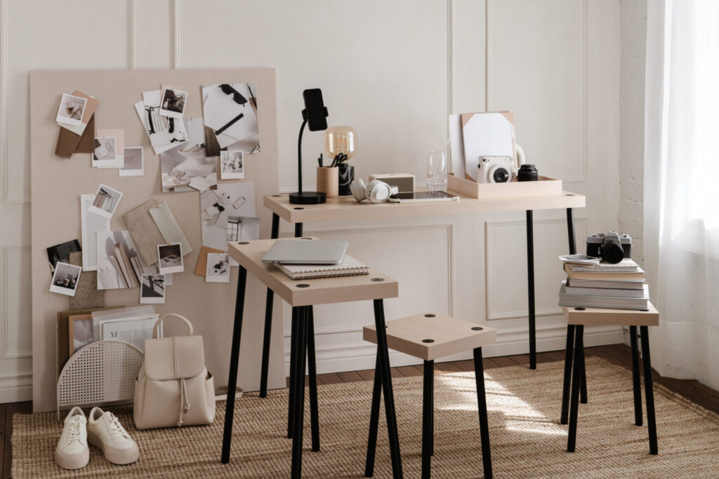 Light-filled creative studio with a reference board, laptop, cameras, notebooks, books, headphones, and neutral accessories.