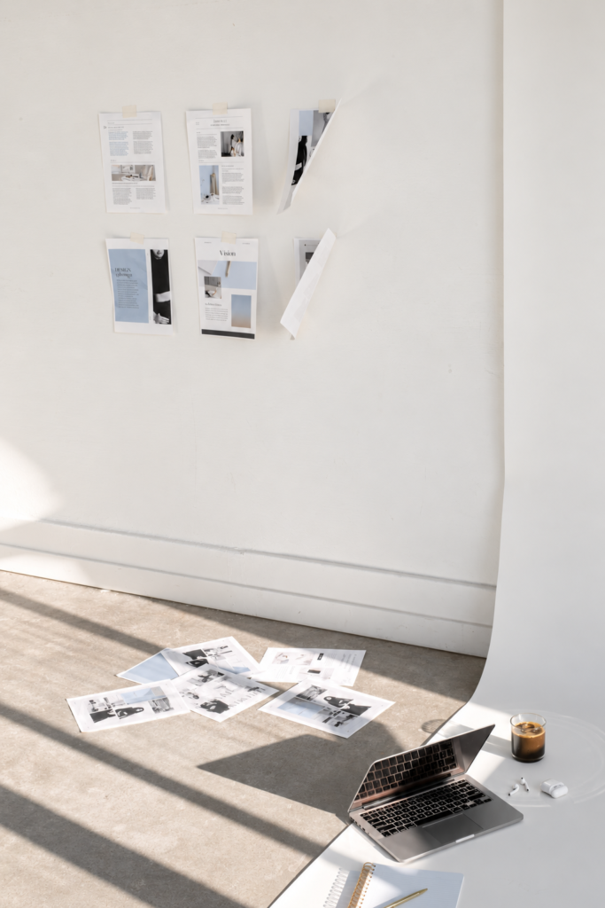 Creative studio with concept pages pinned to a curved wall and a laptop, notebook, coffee, and printed references below.