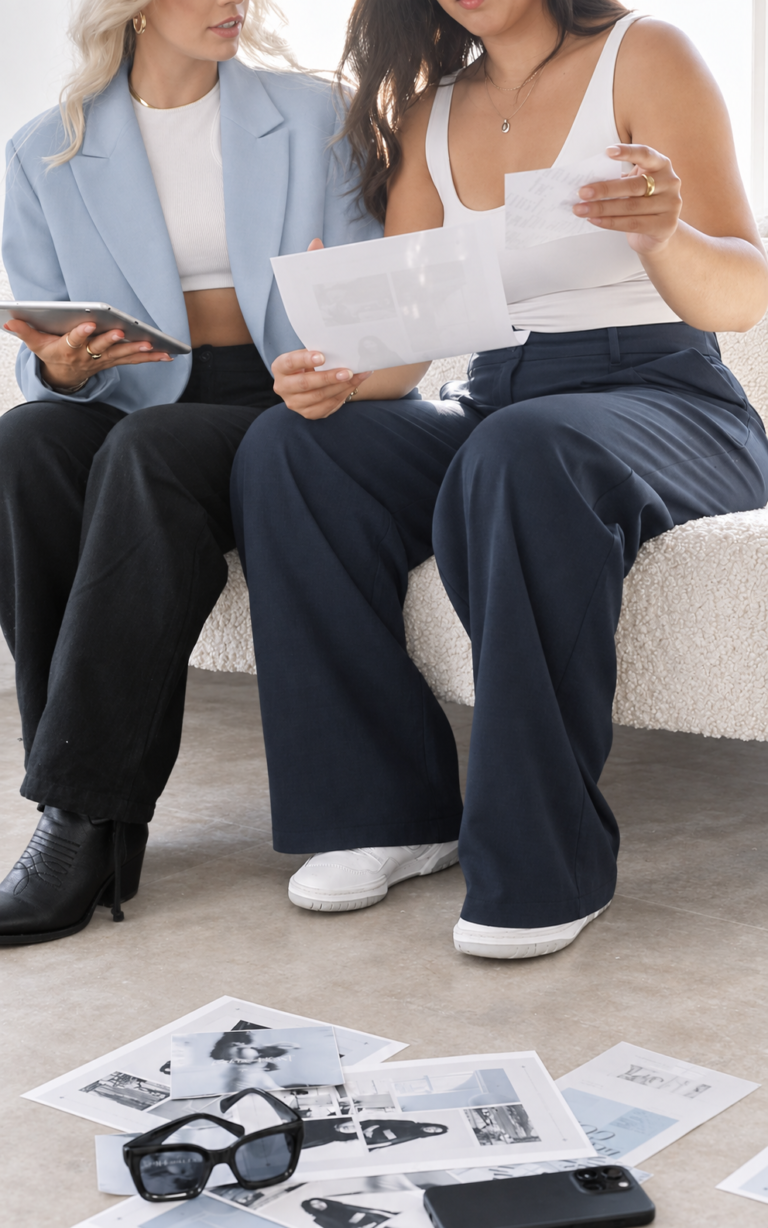 Two women reviewing client onboarding documents and a tablet during a business meeting.