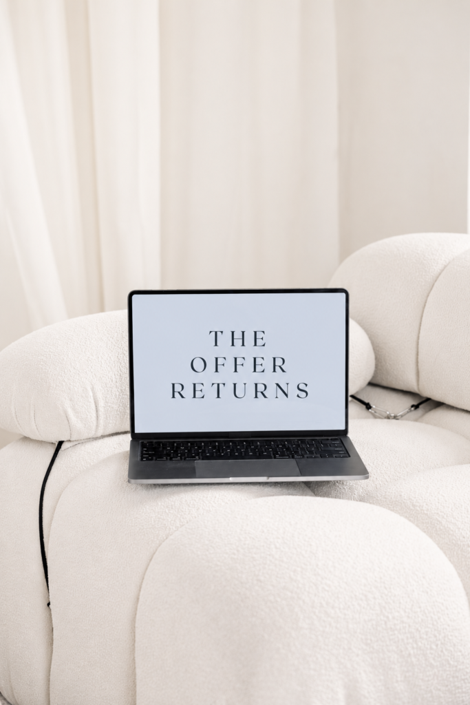Open laptop displaying “The Offer Returns” on sculptural cream chairs.