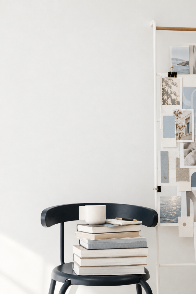 Stack of books and a ceramic cup on a slate chair beside a board of photographs, paper samples, and blue-grey color swatches.