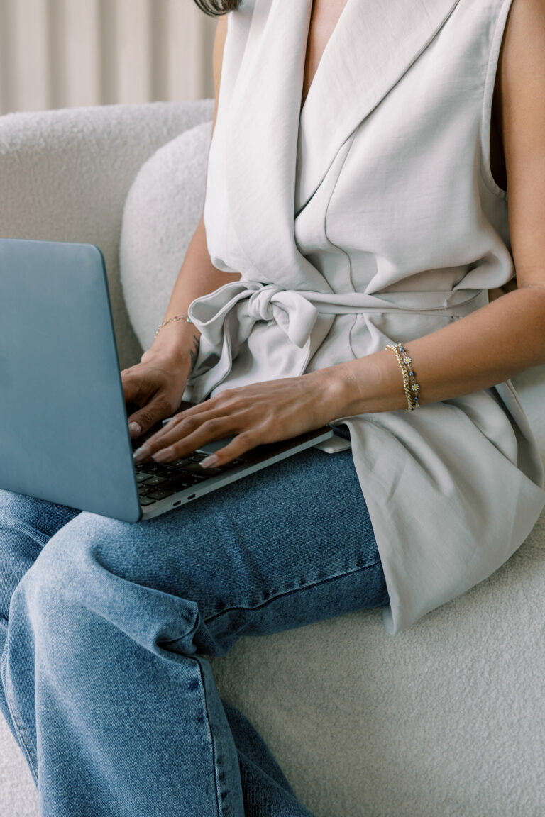 A woman seated in an armchair typing on a laptop.