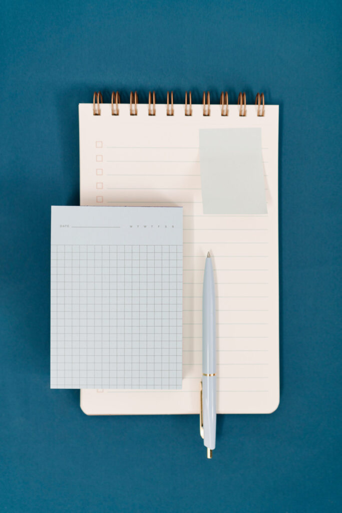 Blue folders, task pads, sticky notes, a ruler, pen, and gold clips arranged on a white surface.