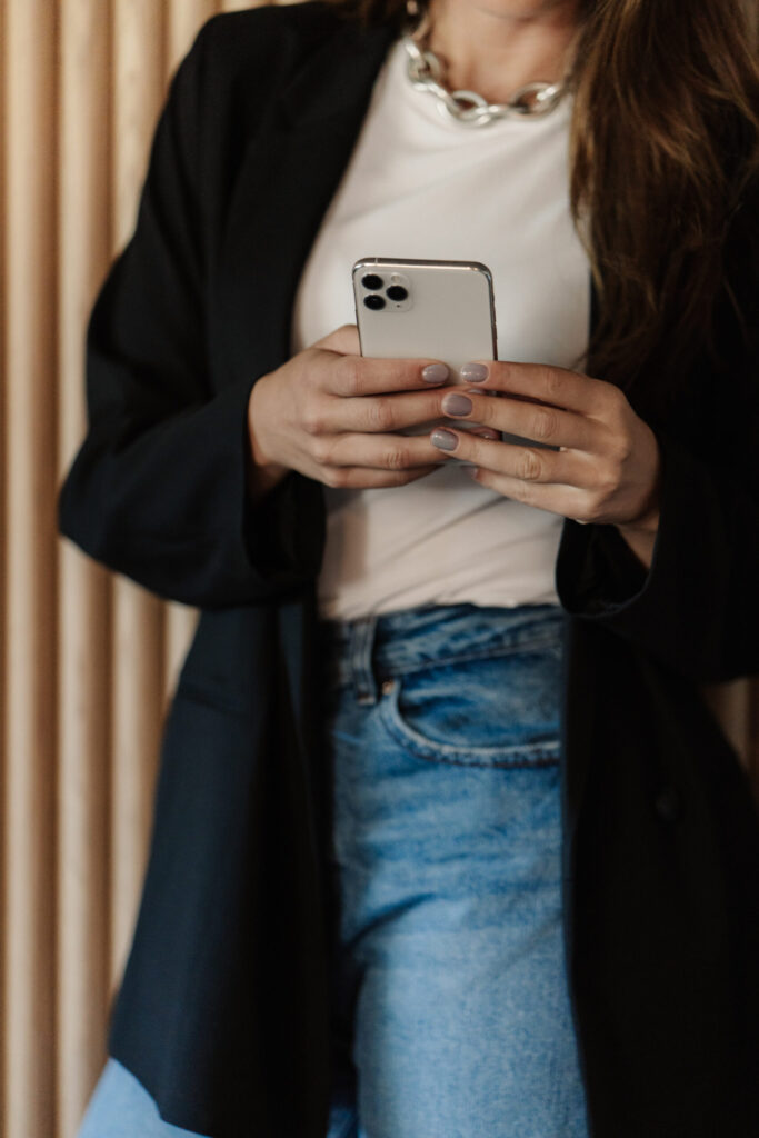 A woman in a black blazer and jeans using a smartphone indoors.