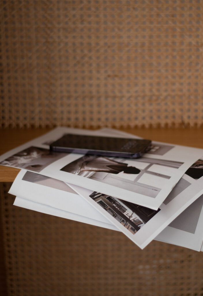 Smartphone resting on a stack of printed photographs arranged on a woven brown chair.