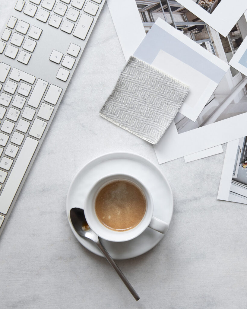 A keyboard, cup of coffee, fabric swatch, color samples, and printed photographs arranged on a desk.