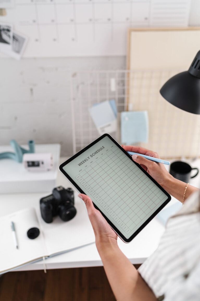 A business owner writing in an open weekly planner beside a laptop and coffee on a softly lit desk.