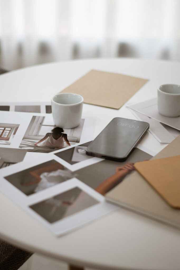 Printed photographs, notebooks, two white cups, and a smartphone arranged across a round white table.