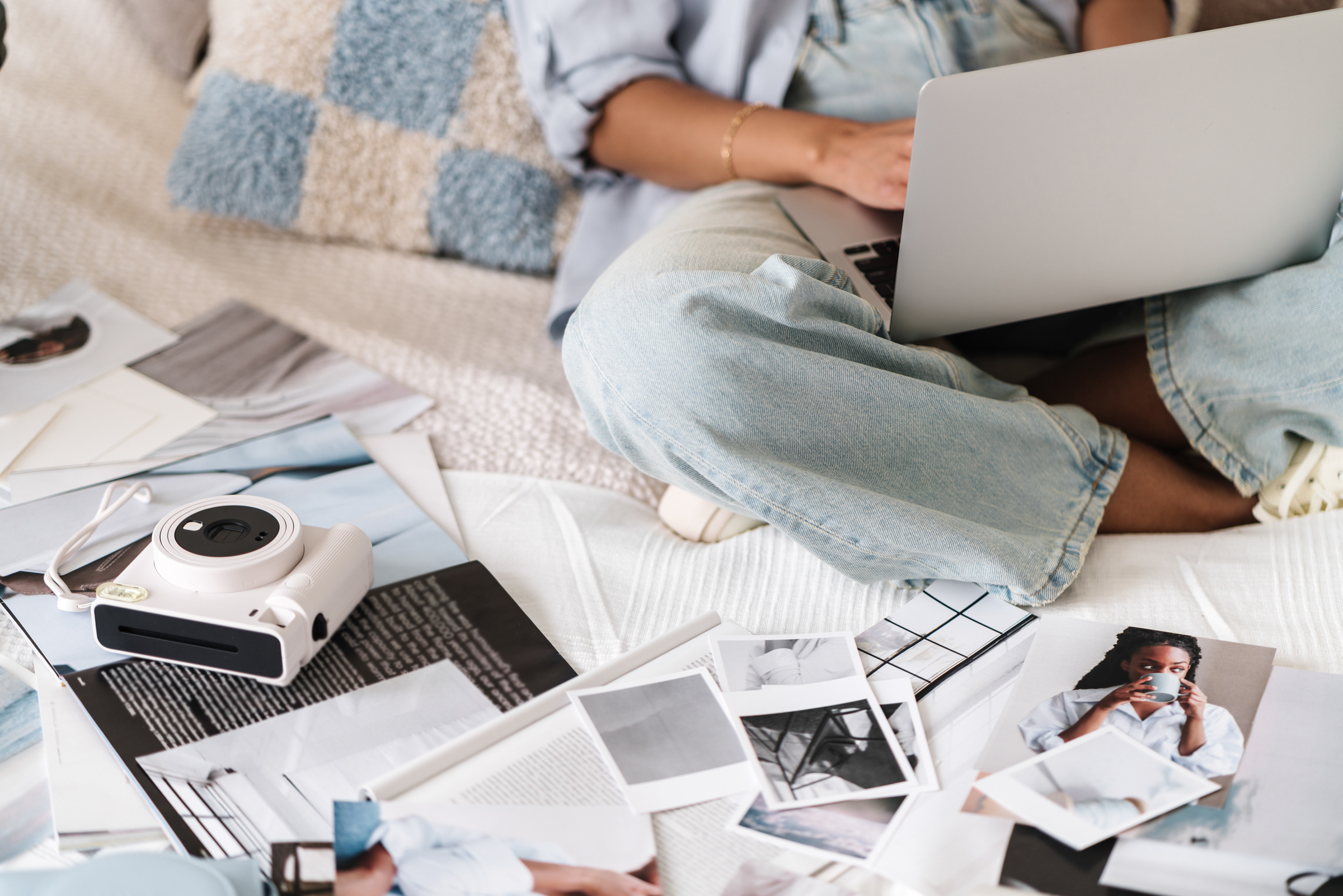 A business owner works on a laptop surrounded by printed photographs and an instant camera.