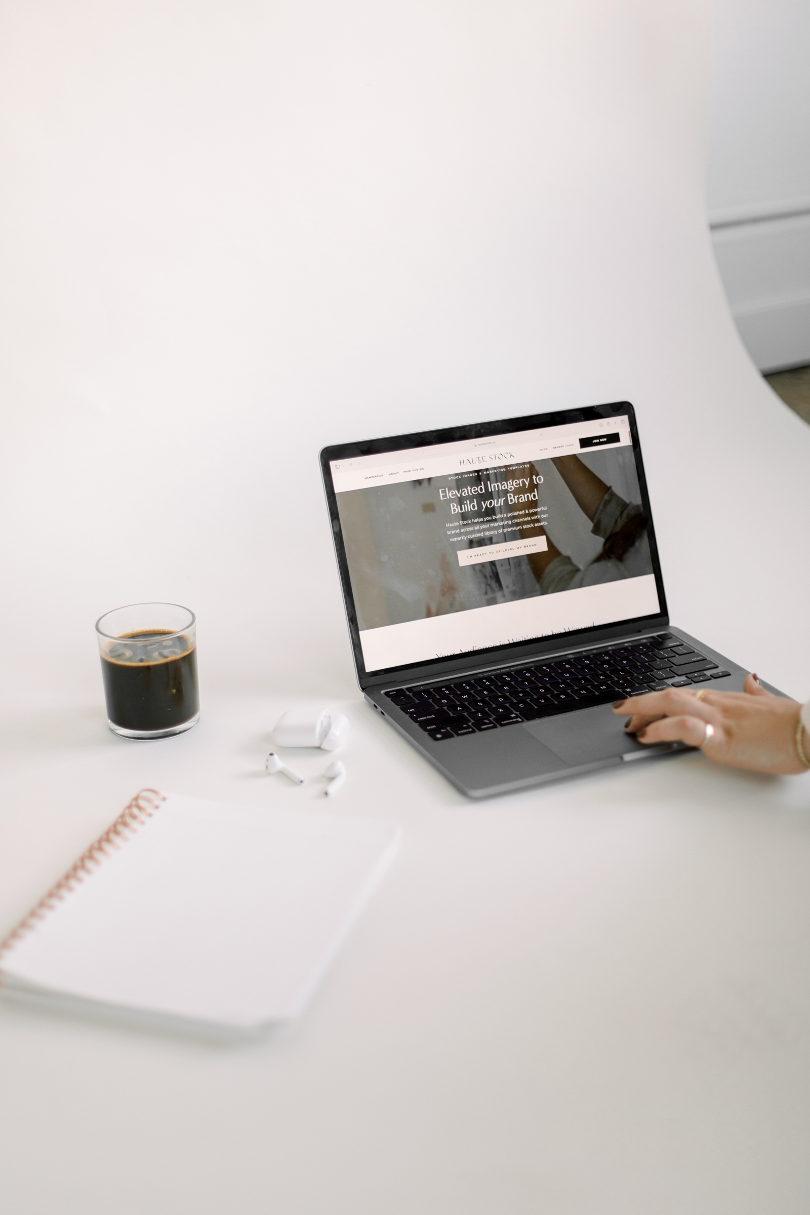 A person reviewing a website on a laptop at a white desk with coffee, earbuds, and a notebook.