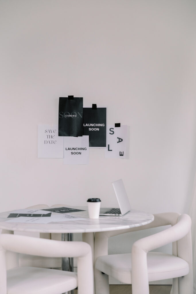 Laptop and coffee on a round table beneath a wall display of launch announcement drafts.